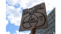 Hand holding sign that says "Keep the same energy for both" with a venn diagram of "racism" and "Covid19" with "I can't breathe" in the center against a backdrop of blue sky with clouds