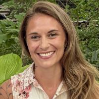Annie Robinson, MS, instructor for Creativity as Essential Clinical Capacity, smiling outdoors surrounded by green foliage.