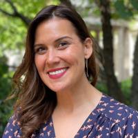 A headshot of Narrative Medicine Program Manager Aly Tadros standing before a tree in a navy dress, smiling